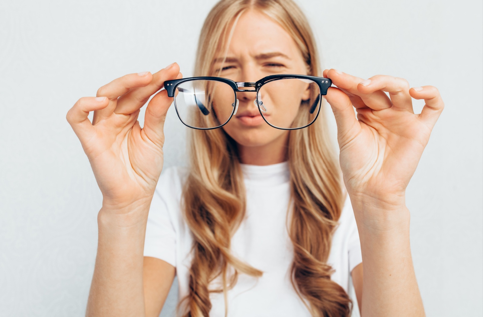 A person holding their glasses in front of their. face as they struggle to see clearly.